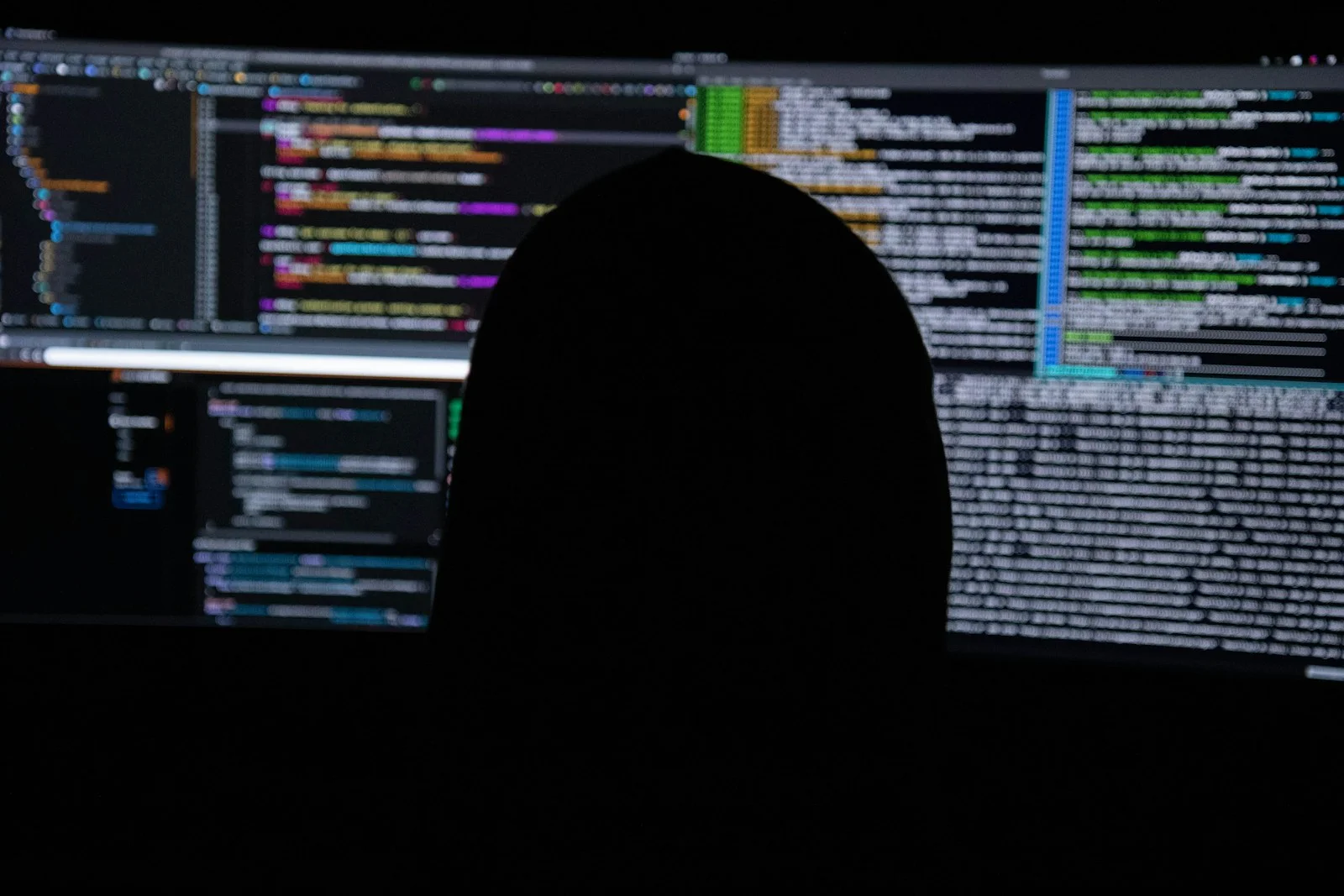 Silhouette in front of monitors full of code during incident response