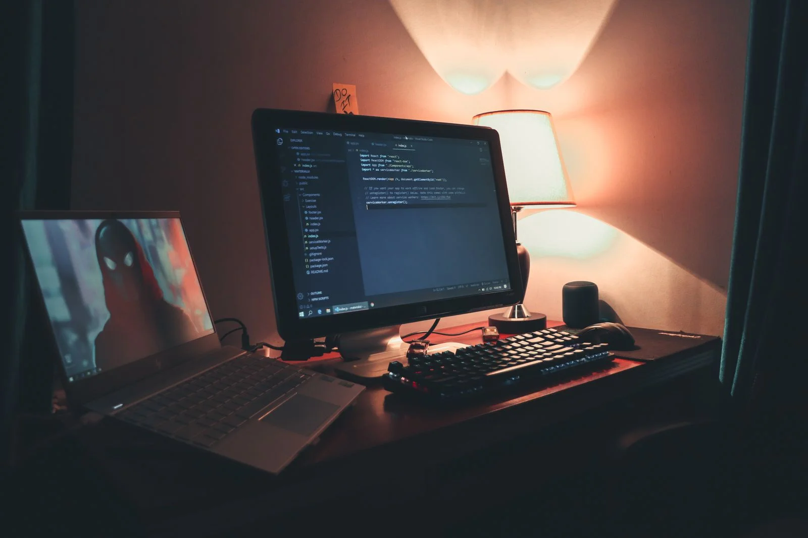 Night-time desk setup: a monitor with code, a laptop and a desk lamp